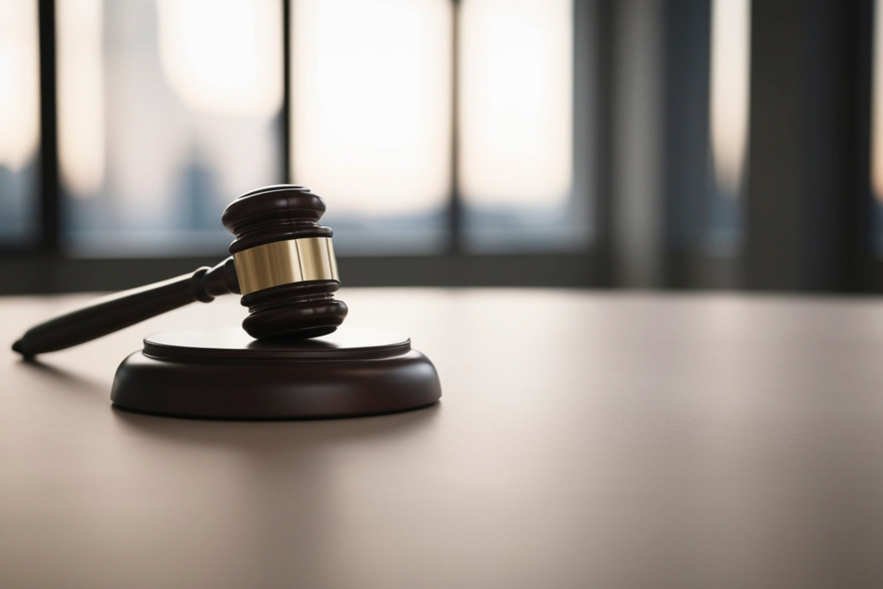 A wooden judge's gavel resting on a courtroom table near a window